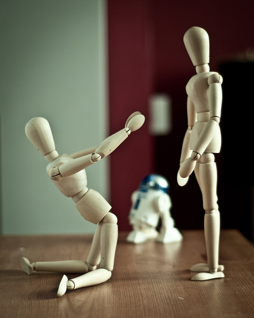 A photograph of two human figures. One is on its knees pleading with the other one