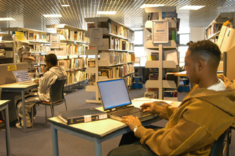 A photograph of a male student working on a laptop, in a library