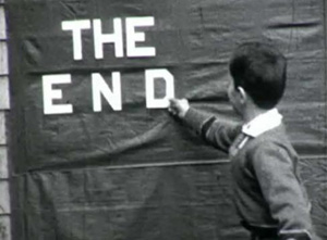 Boy pinning the words “The End” on a wall, black and white film.