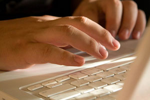 A photograph of hands typing on a laptop computer keyboard.