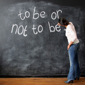 A photograph of a woman writing “To be or not to be” on a chalk board.