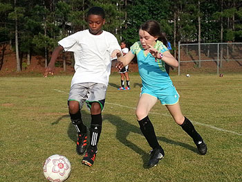 A photograph of a young male and female players practicing their soccer skills.