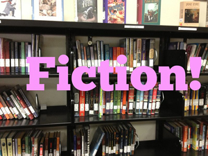 A photograph of books in a library with the word “Fiction” in the middle of the frame.