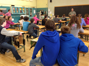 A photograph of students sitting in a classroom listening to a teacher.