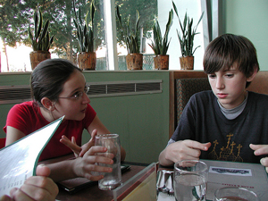 A photograph of a girl having an animated conversation with a boy. They are seated at a table.