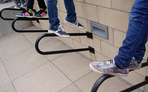A photograph of bike racks at a school. Kids are standing on them, but all that is visible are their legs and shoes.