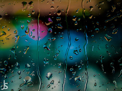 A photograph of raindrops on glass at night with blurred lights in the background.