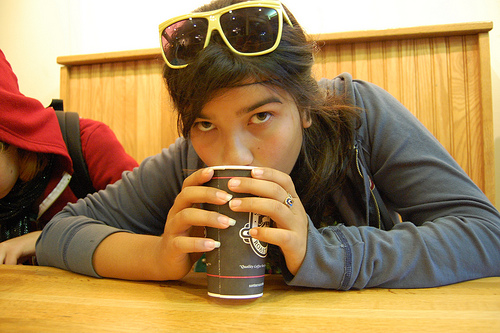 A photograph of a young woman sipping from a cup.