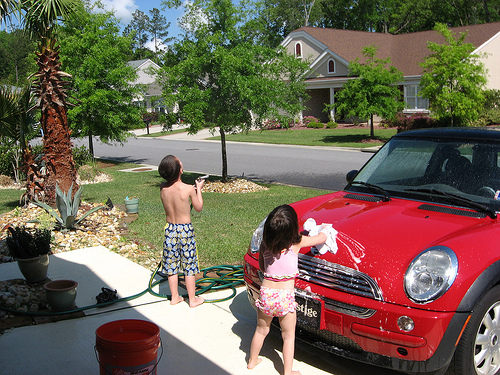 A photograph of two young children washing a car in the driveway.