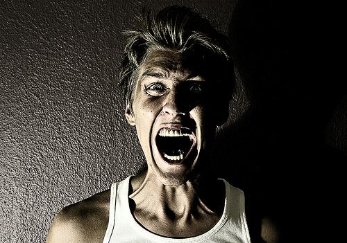 A photograph of a man standing with his back against the wall. He is screaming like he is terrified of something.