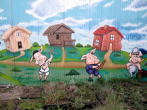 A photograph of a painting of the three little pigs and their houses standing side by side.