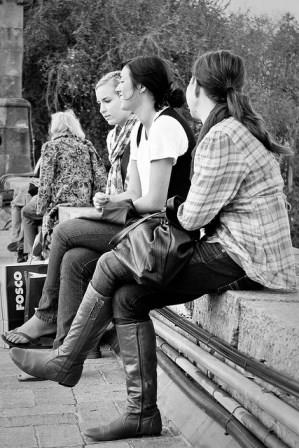 A photograph of a three teen aged girls talking about something while sitting outside