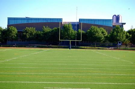 A photograph of a goal post on a football field near a school