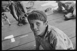 A photograph of a young boy sitting on a porch playing with other children. The photo is from the 1930s.