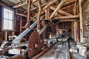 A photograph of the interior of a saw mill. There are conveyor belts and a large mounted saw