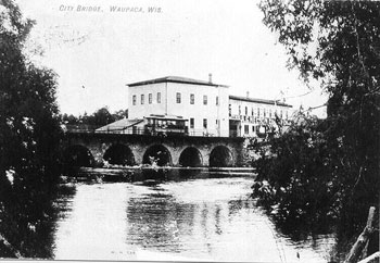 image of an old lumber mill, several big white buildings, overlooking a river