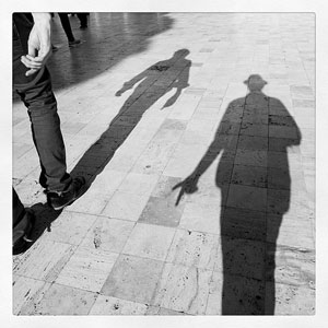 A photograph of two people’s shadows on a sidewalk