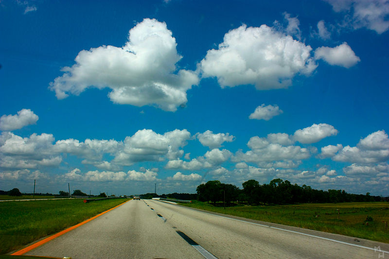 A photograph of a country road on a partly cloudy day.
