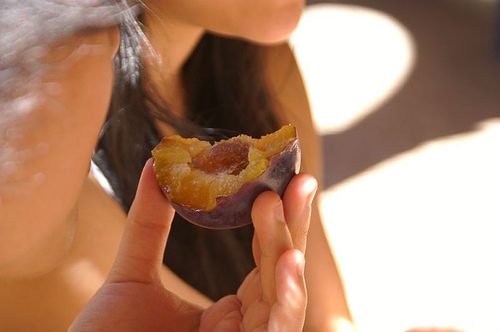 A person holding up a half-eaten plum.