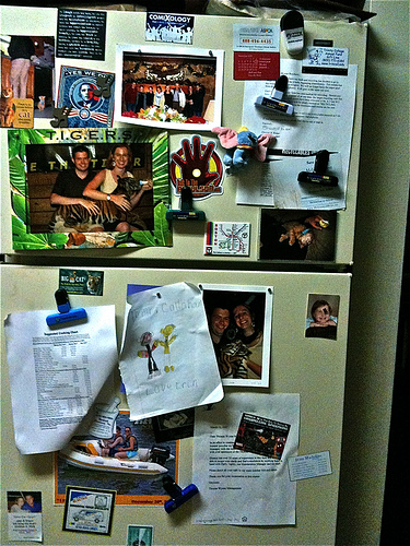 A photograph of a refrigerator door covered with notes, drawing , and other items.