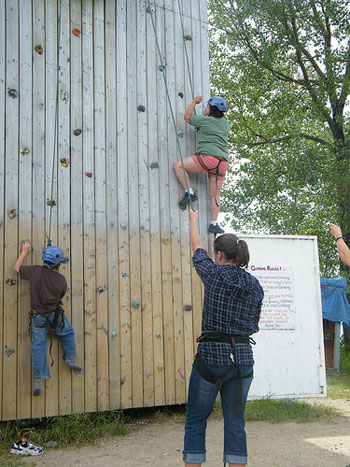 A photograph of two students rock climbing on a wall while an instructor looks on.