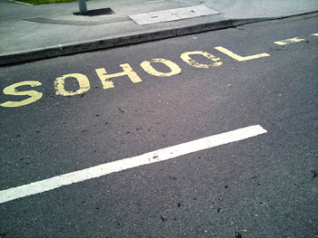 A photograph of a street outside a school with the word “Sohool” painted on it