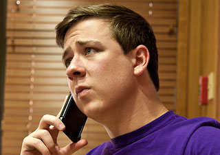 A photograph of a young man talking on the telephone with a serious look on his face