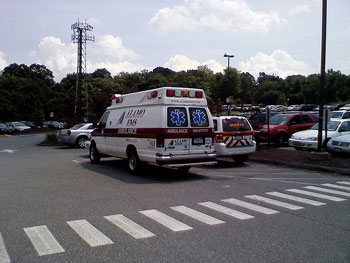 A photograph of an ALAMO EMS ambulance and an additional emergency vehicle driving through a parking lot