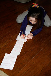 A photograph of a girl sitting on the floor and writing out a long list of some sort
