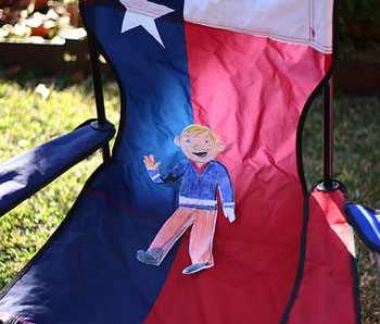 photo the paper cut-out character Flat Stanley sitting in a camping chair designed with the colors of the Texas flag