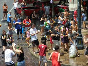 A photograph of a crowd of people on a street corner involved in an giant water balloon fight.