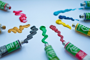 A photograph of several tubes of paint with paint representing each squirted out on paper in front of the tube