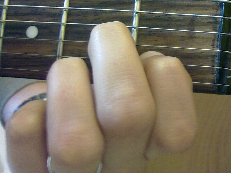 A photograph of a person’s fingers on a guitar fret playing a chord