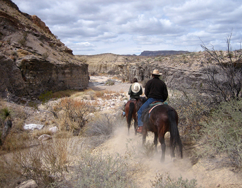 photo of two people riding horses through dusty, rocky terrain
