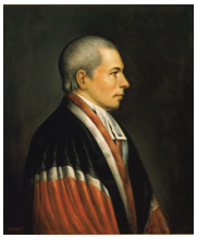 A gray-haired man seated wearing a red and black striped robe.
