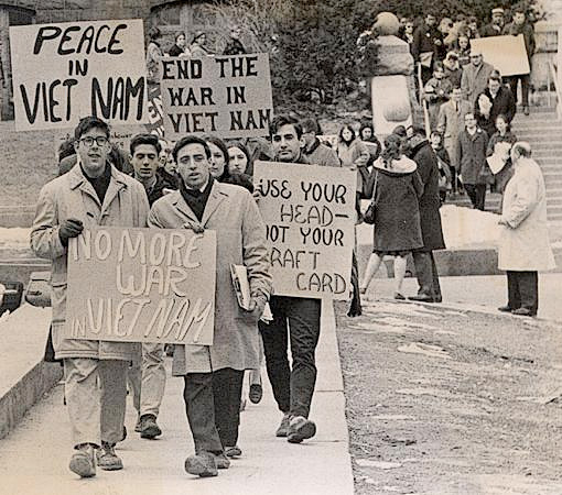 A group of student protesters in the 1960s carrying signs that say Peace in Vietnam, End the War in Vietnam, No More War in Vietnam.