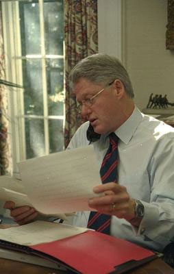 Image of President Clinton talking on the phone while holding papers in his hands.