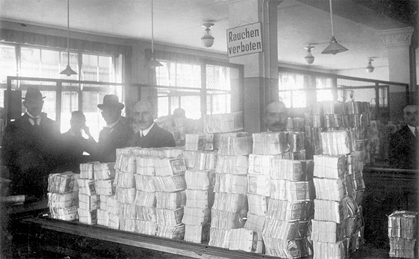 A photograph of large stacks of German Marks (paper money) sitting on countertops with several men standing behind them.