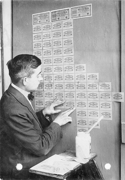 A photograph of a man pasting German Marks (paper money) onto a door or wall.